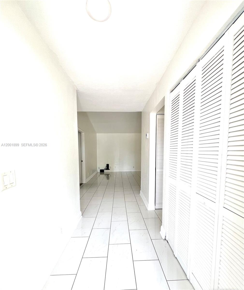 A hallway with white tile flooring leads to an open living area with louvered closet doors — 6109 NW 171st St, Hialeah FL 33015, HIALEAH, FL