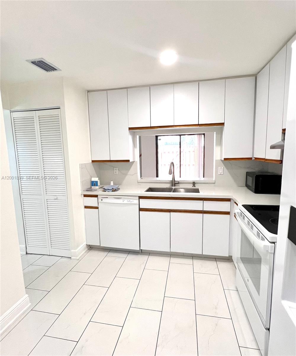 A kitchen features white cabinets with wood trim, white countertops, and light-colored tile flooring — 6109 NW 171st St, Hialeah FL 33015, HIALEAH, FL