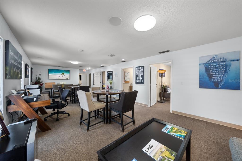 An office space features multiple desks, chairs, and motivational wall art on a carpeted floor — 1211 12TH STREET, ST CLOUD, FL