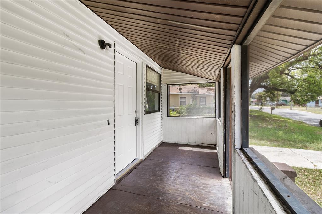 A covered porch with white siding, a white door, and a dark wood-look floor — 638 W 8TH STREET, LAKELAND, FL