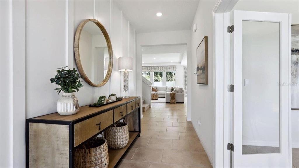 A bright entryway features a wood and metal console table, a round mirror, and tile flooring — 35608 LOWERY TRAIL, ZEPHYRHILLS, FL