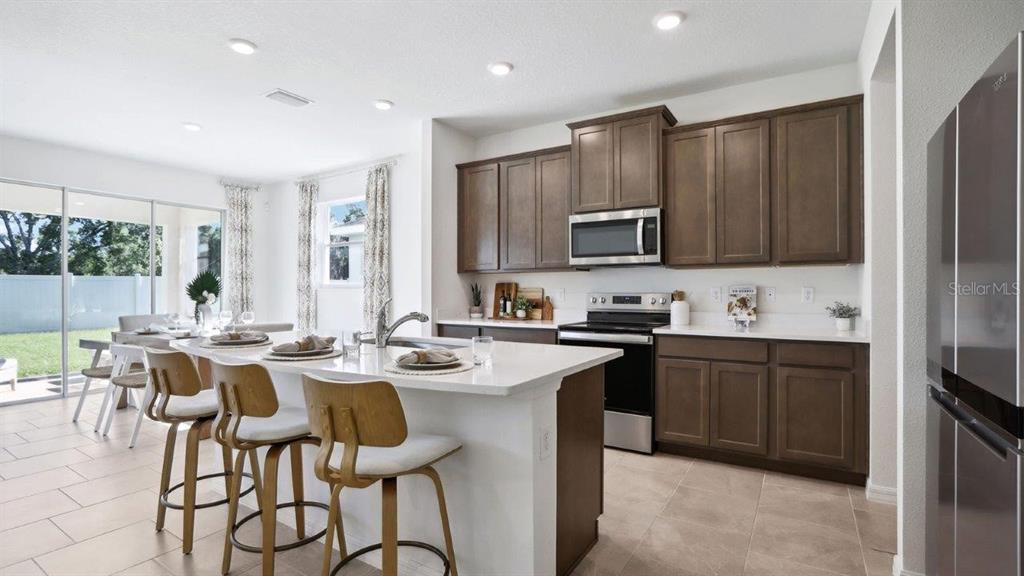 A modern kitchen features dark wood cabinets, white countertops, a center island, and stainless appliances — 35608 LOWERY TRAIL, ZEPHYRHILLS, FL