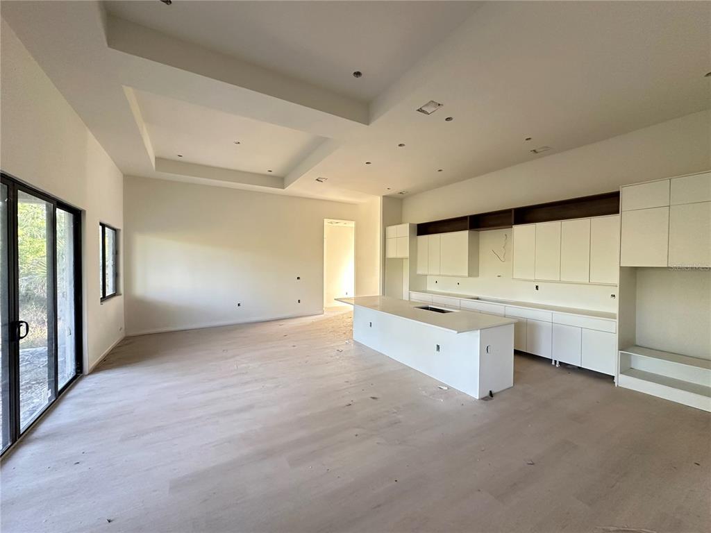 A modern, unfinished kitchen features white cabinetry, a large center island, and light wood flooring — 34 LONGLEY DRIVE, PORT CHARLOTTE, FL