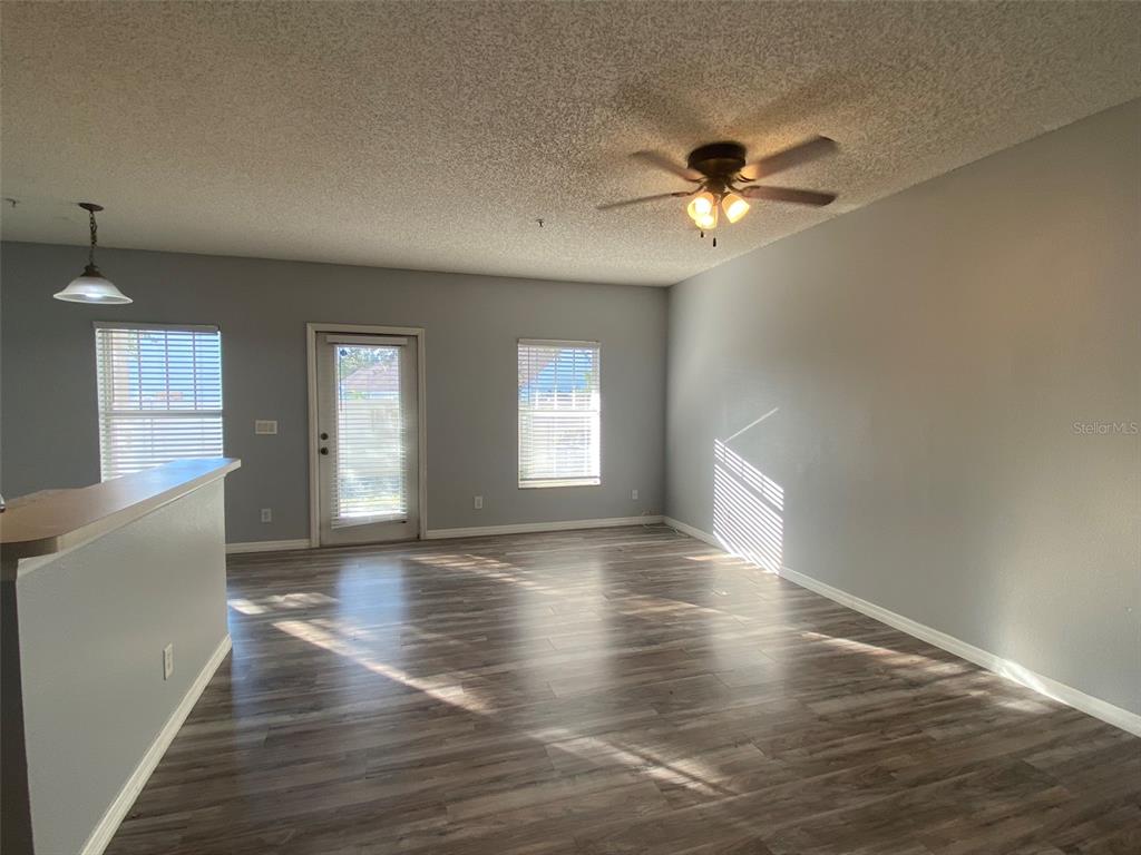 An empty living room features gray walls, wood-look flooring, a ceiling fan, and sliding doors — 2076 CYPRESS BAY BOULEVARD, KISSIMMEE, FL
