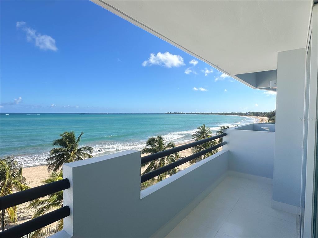 A balcony with white walls and black railings overlooks a sandy beach and the ocean — 7043 Horizonte St. PLAYA DORADA UNIT 602A, CAROLINA, PR