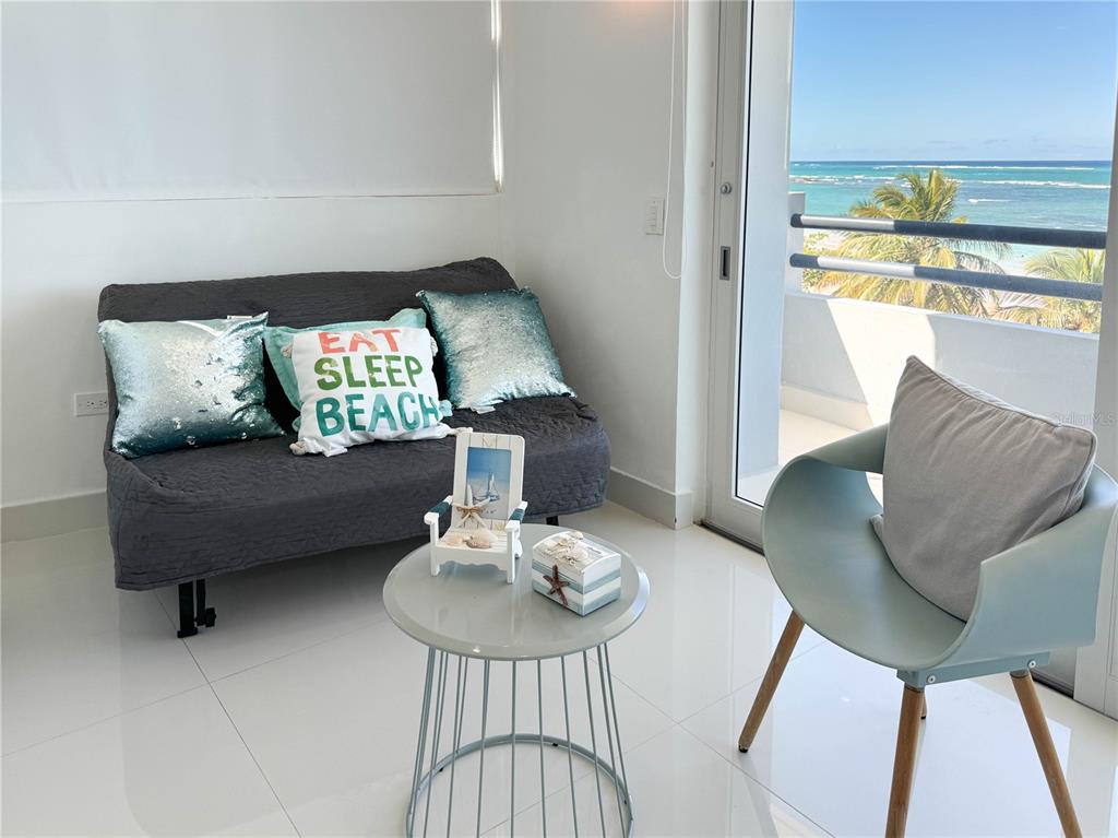 A living area features a gray sofa, a small round table, and a balcony view — 7043 Horizonte St. PLAYA DORADA UNIT 602A, CAROLINA, PR