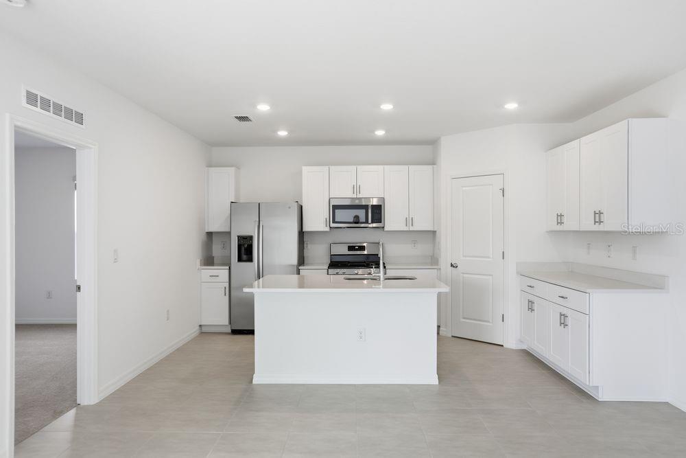 A modern kitchen features white cabinetry, stainless steel appliances, a center island, and tile flooring — 752 HAZELWOOD COURT, HAINES CITY, FL