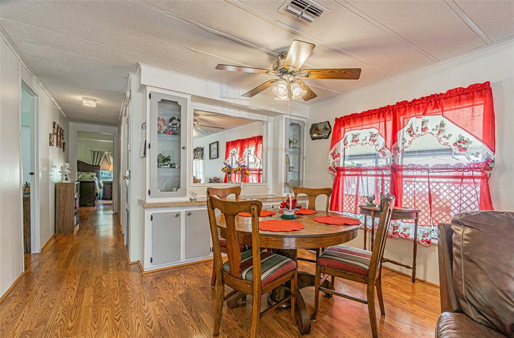 A dining area features a round wooden table, chairs, built-in cabinetry, and red window curtains — 39353 SYCAMORE LANE, ZEPHYRHILLS, FL