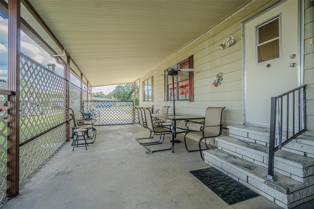 A covered concrete porch features outdoor furniture, lattice privacy screens, and steps to a door — 39353 SYCAMORE LANE, ZEPHYRHILLS, FL