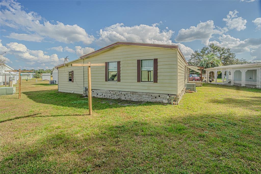 The exterior of a light-colored mobile home features a stone-patterned skirting and a clothesline — 39353 SYCAMORE LANE, ZEPHYRHILLS, FL