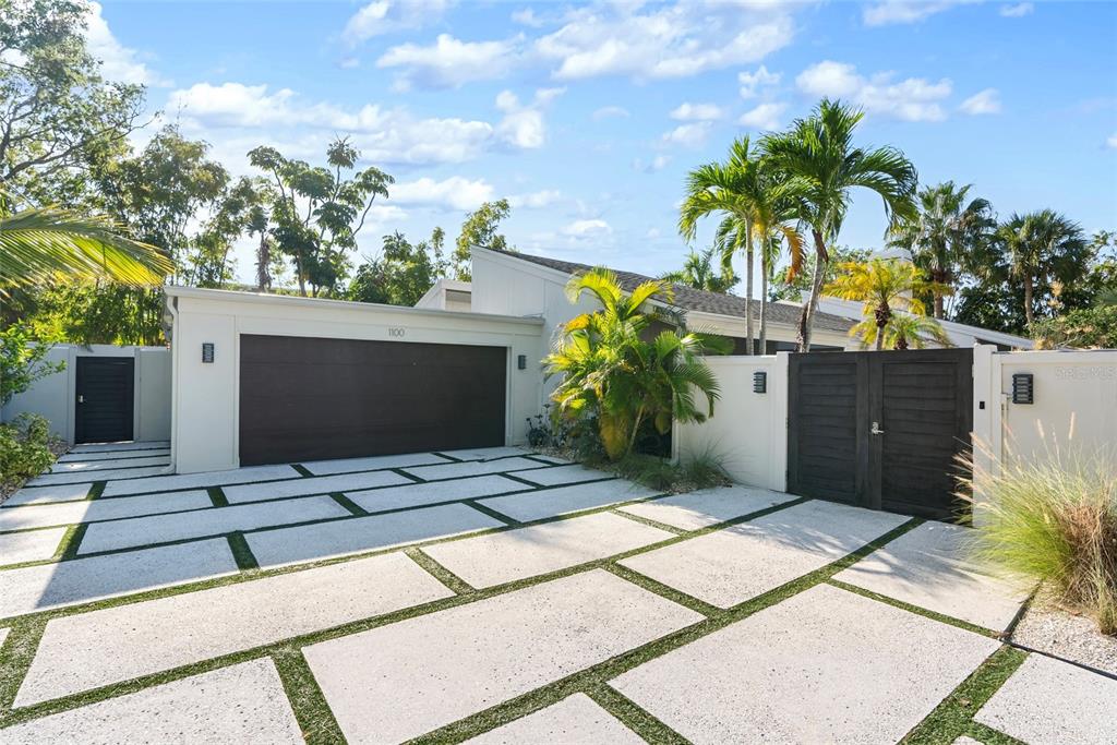 A modern house exterior features a paved driveway with grass strips and a dark garage door — 1100 WESTWAY DRIVE, SARASOTA, FL