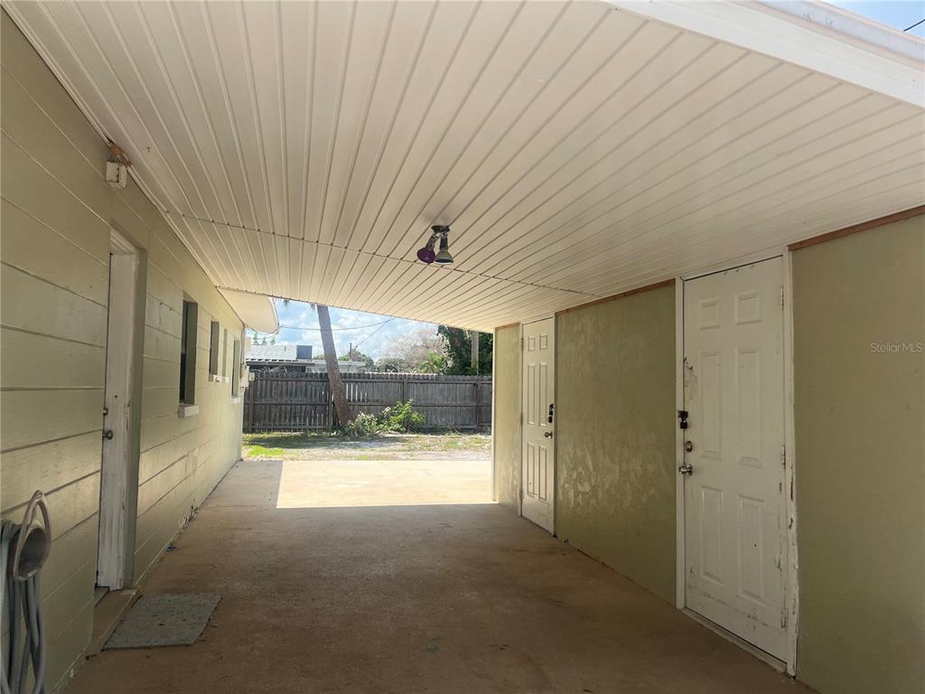 A covered carport with a concrete floor, white ceiling, and two white exterior doors — 813 8TH STREET, MERRITT ISLAND, FL