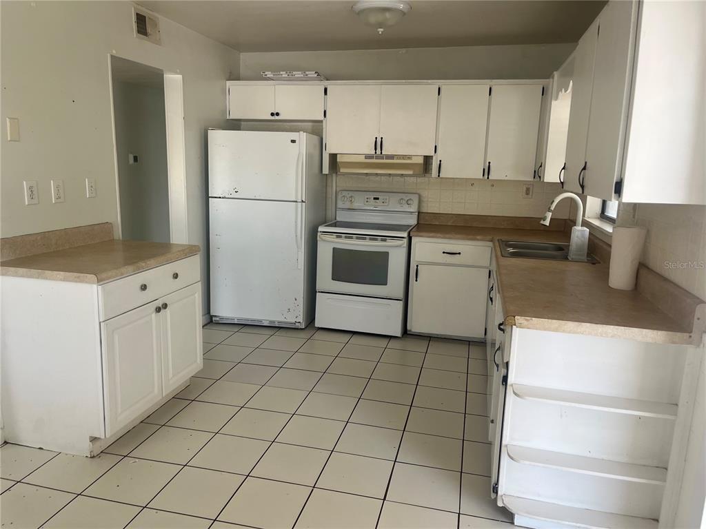 A kitchen with white cabinets, white appliances, tan laminate countertops, and white tile flooring — 813 8TH STREET, MERRITT ISLAND, FL