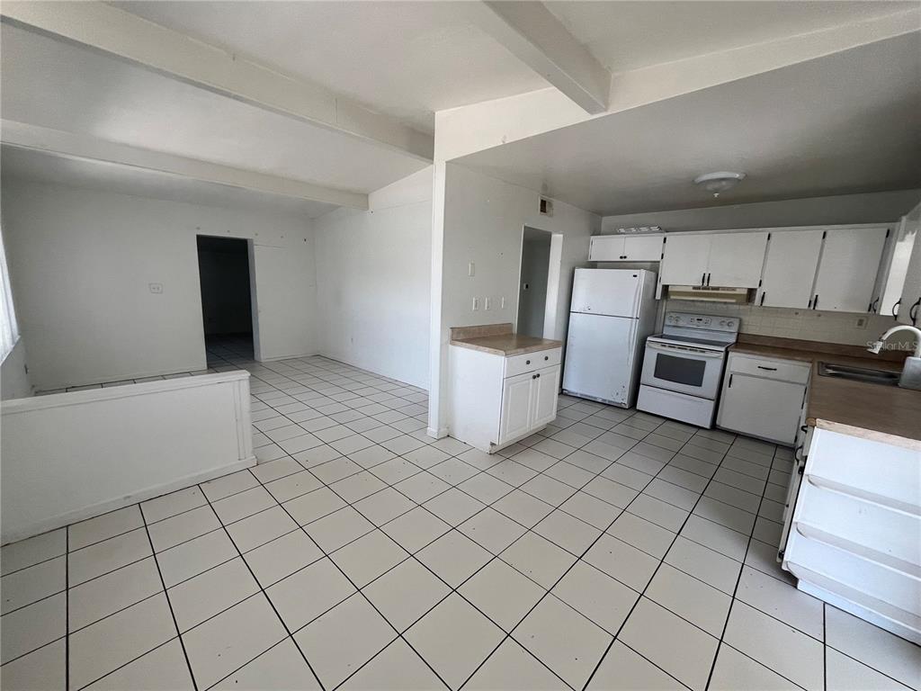 An open-concept kitchen and living area features white cabinets, white appliances, and tiled flooring — 813 8TH STREET, MERRITT ISLAND, FL