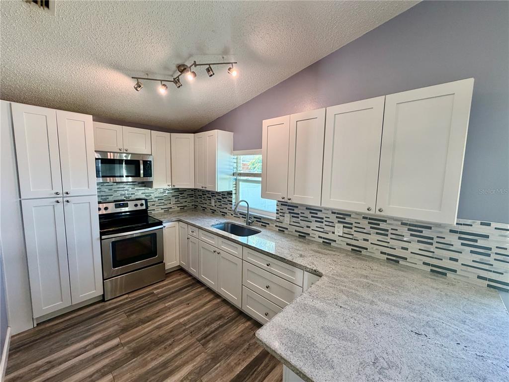 A kitchen features white cabinets, granite countertops, stainless steel appliances, and a tiled backsplash — 2604 W KIRBY STREET, TAMPA, FL