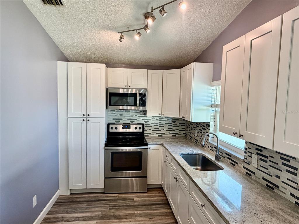A kitchen features white cabinets, stainless steel appliances, granite countertops, and a tiled backsplash — 2604 W KIRBY STREET, TAMPA, FL