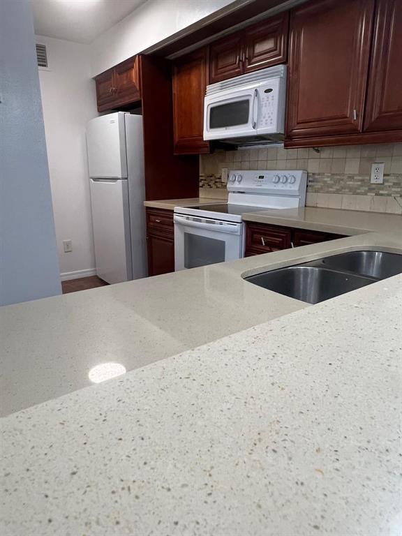 A kitchen features cherry wood cabinets, white appliances, and light-colored speckled countertops — 18840 NW 57th Avenue Unit 101, Hialeah FL 33015, HIALEAH, FL