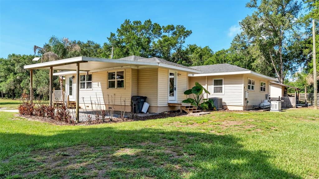 The exterior of a light-colored, single-story house features a covered patio and surrounding lawn — 5275 GREEN POND ROAD, POLK CITY, FL