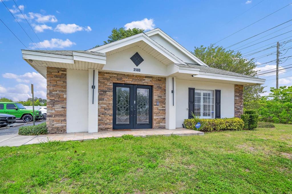 A single-story commercial building features a stone facade, double glass entry doors, and white siding — 2500 SUNSET POINT ROAD, CLEARWATER, FL