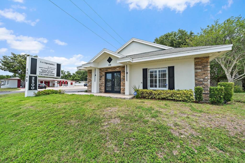 A single-story commercial building with a stone facade, black shutters, and a prominent signage pillar — 2500 SUNSET POINT ROAD, CLEARWATER, FL