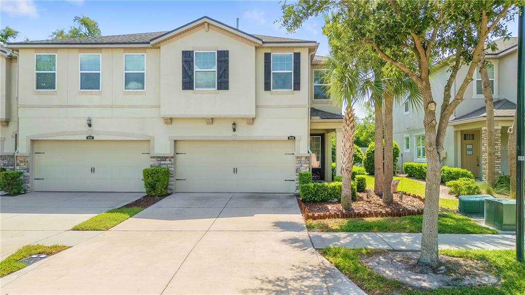 A two-story townhouse with a two-car garage, beige stucco siding, and a small front yard — 10316 HOLSTEIN EDGE PLACE, RIVERVIEW, FL