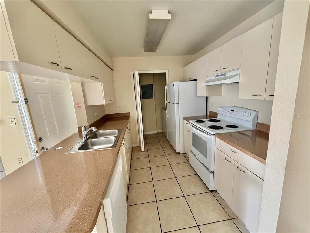 A galley-style kitchen features white cabinets, tan countertops, a white stove, and tile flooring — 2550 N ALAFAYA TRAIL UNIT 3103, ORLANDO, FL