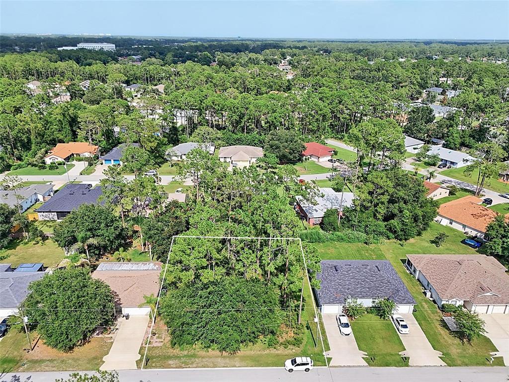 An aerial view shows a vacant, tree-covered residential lot situated between two single-family homes — 30 WELLWOOD LANE, PALM COAST, FL