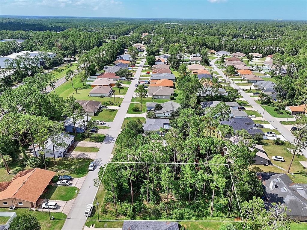 An aerial view shows a vacant, tree-covered residential lot outlined in white within a neighborhood — 30 WELLWOOD LANE, PALM COAST, FL