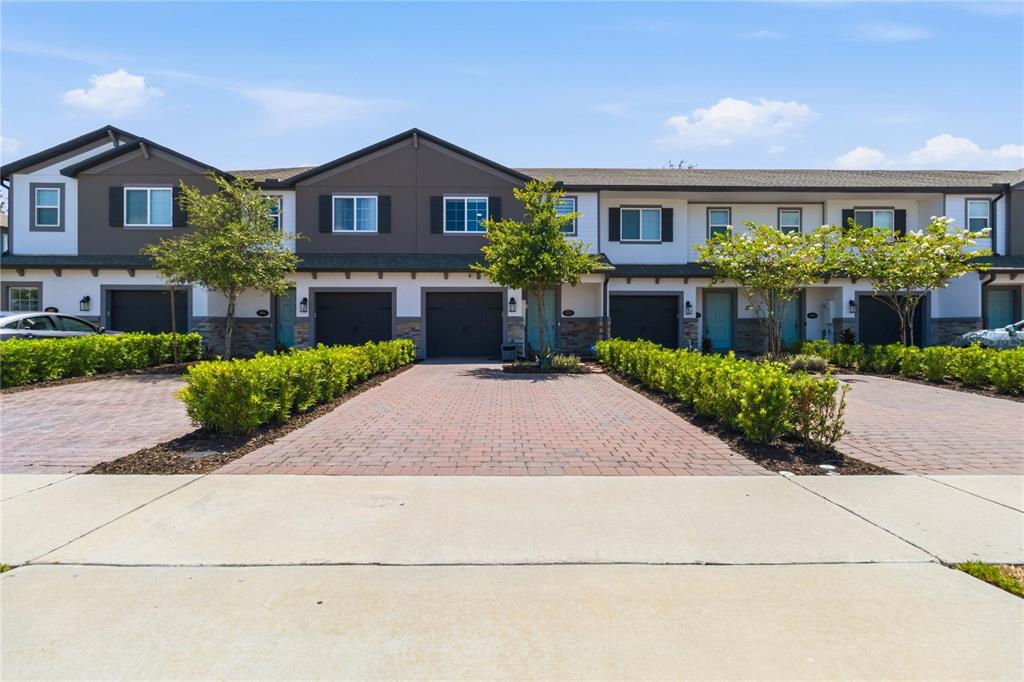 A row of multi-story townhomes features brick driveways, attached garages, and manicured landscaping — 385 CAPE HONEYSUCKLE PLACE, SANFORD, FL
