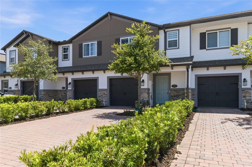 A row of two-story townhomes with dark garage doors, stone accents, and paved driveways — 385 CAPE HONEYSUCKLE PLACE, SANFORD, FL