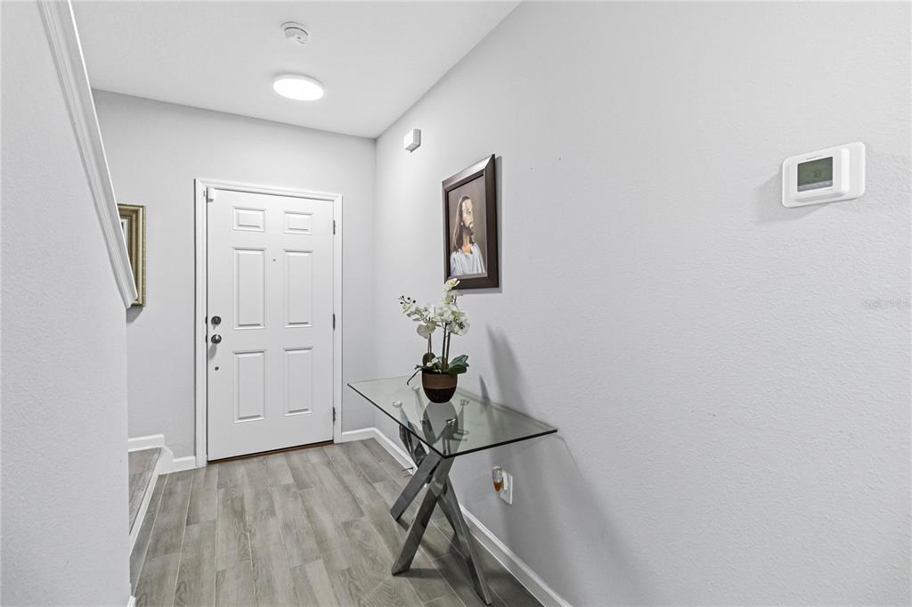 A bright entryway features light wood-look flooring, a glass console table, and a white door — 385 CAPE HONEYSUCKLE PLACE, SANFORD, FL