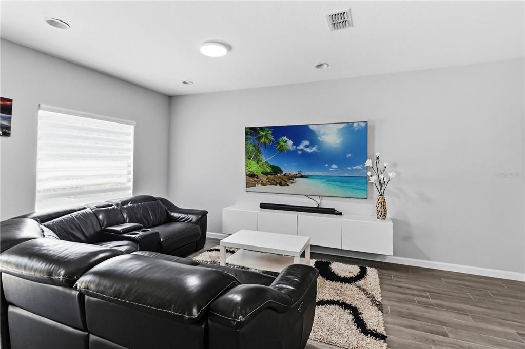 A living room features a black leather sectional, a wall-mounted television, and a white console — 385 CAPE HONEYSUCKLE PLACE, SANFORD, FL