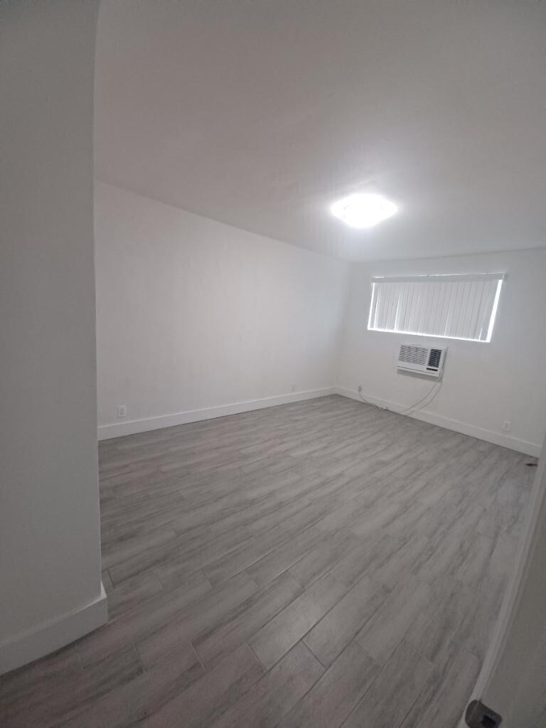An empty room features light gray wood-look flooring, white walls, and a window air conditioner — 24 SW 13th Street # 5, Dania Beach FL 33004, DANIA BEACH, FL