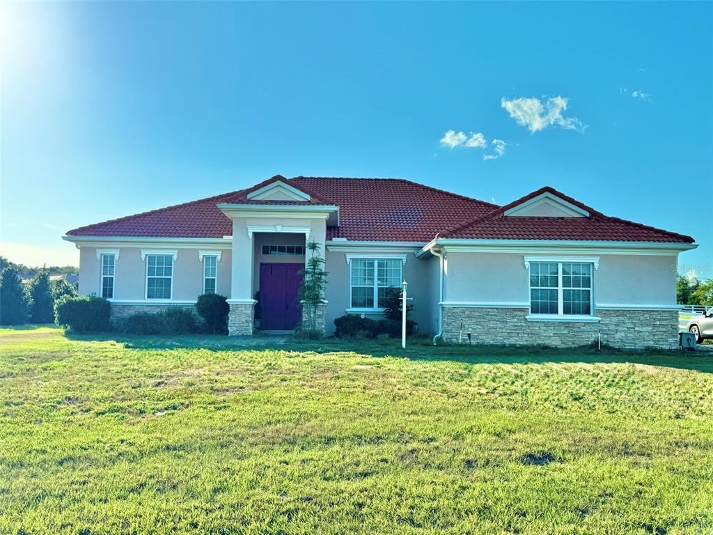 A single-story house with a red tile roof, stone accents, and a purple front door — 56 S NEEDLES POINT, INVERNESS, FL