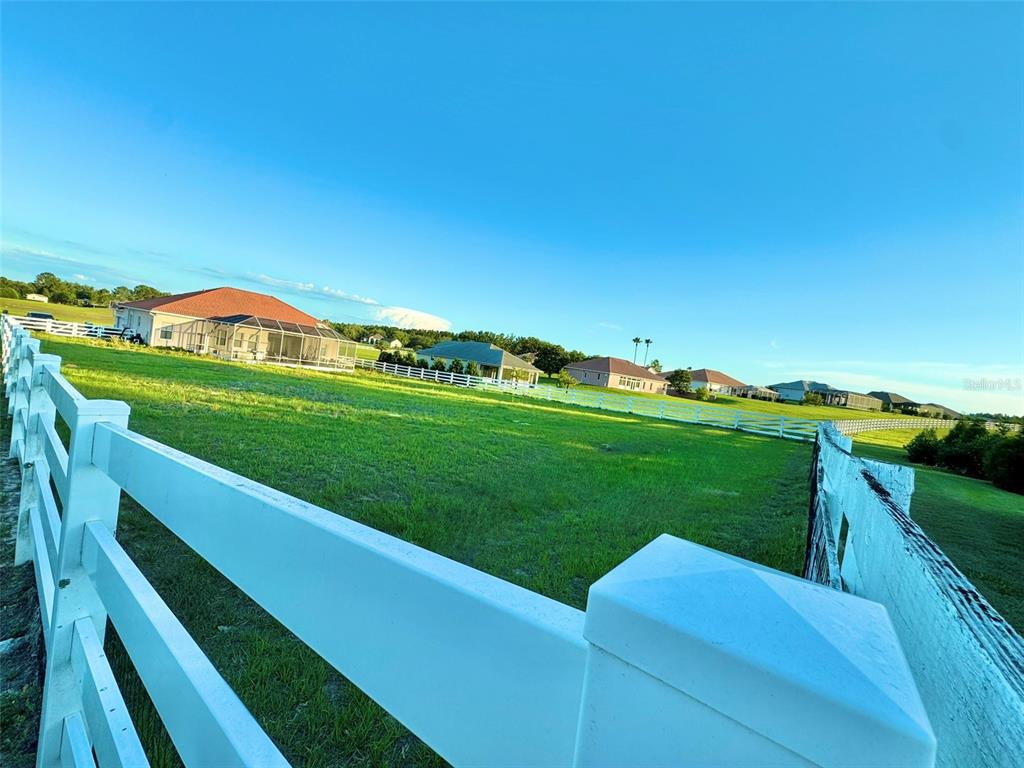 A white rail fence encloses a large, grassy field with several houses in the background — 56 S NEEDLES POINT, INVERNESS, FL
