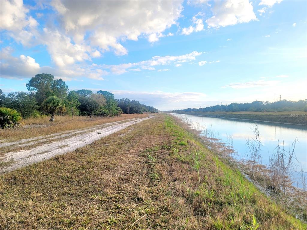 A dirt path runs alongside a canal bordered by grassy banks and trees under a sky — 141 NAPLES AVENUE S, LEHIGH ACRES, FL