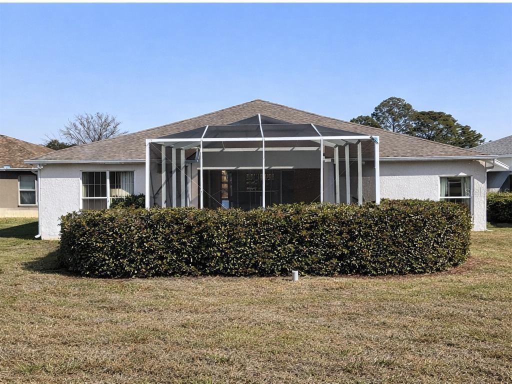 The rear exterior of a single-story house features a screened-in patio and a large hedge — 15296 SW 15TH TERRACE ROAD, OCALA, FL