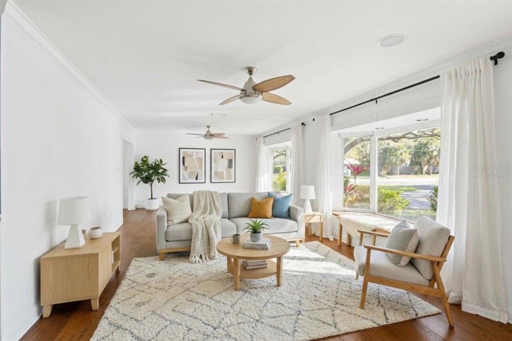 A bright living room features a gray sofa, wooden coffee table, and large bay windows — 201 S SHERRILL STREET, TAMPA, FL