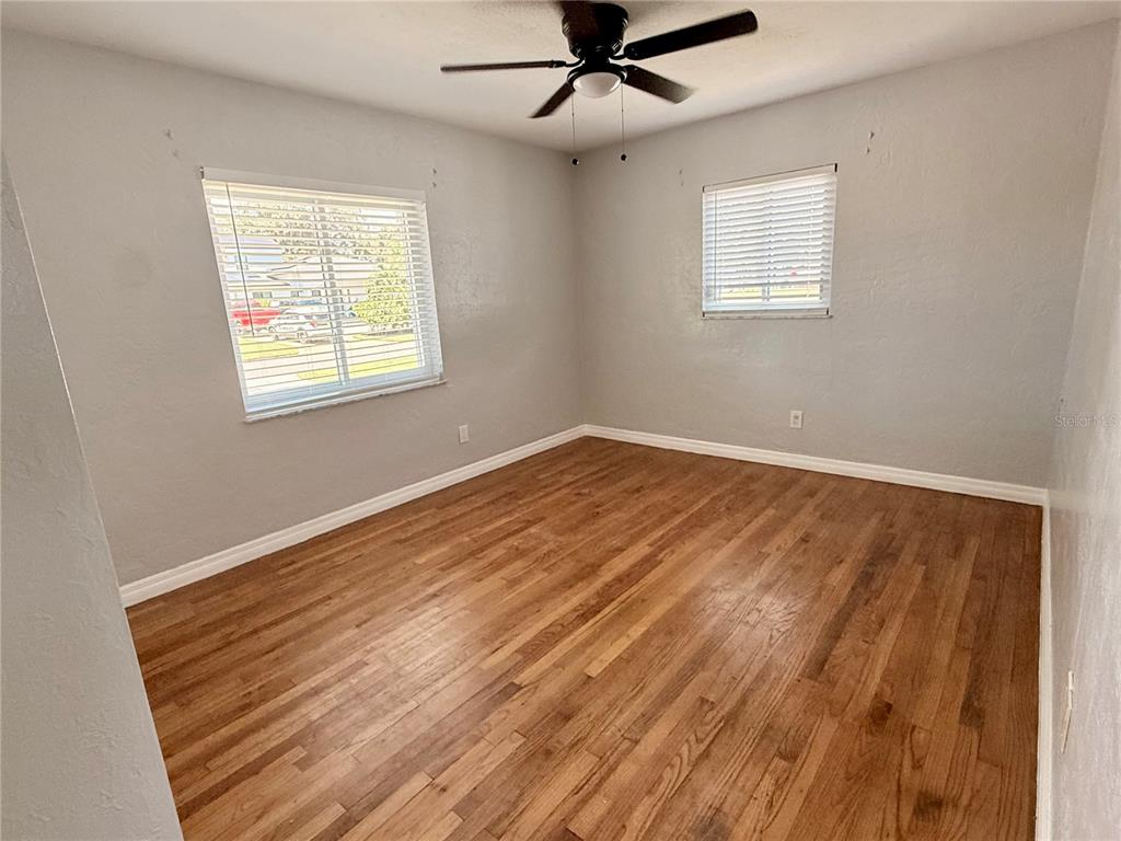 A living room with light blue walls, hardwood floors, and a ceiling fan leads to a kitchen — 4320 YARDLEY AVENUE N, ST PETERSBURG, FL