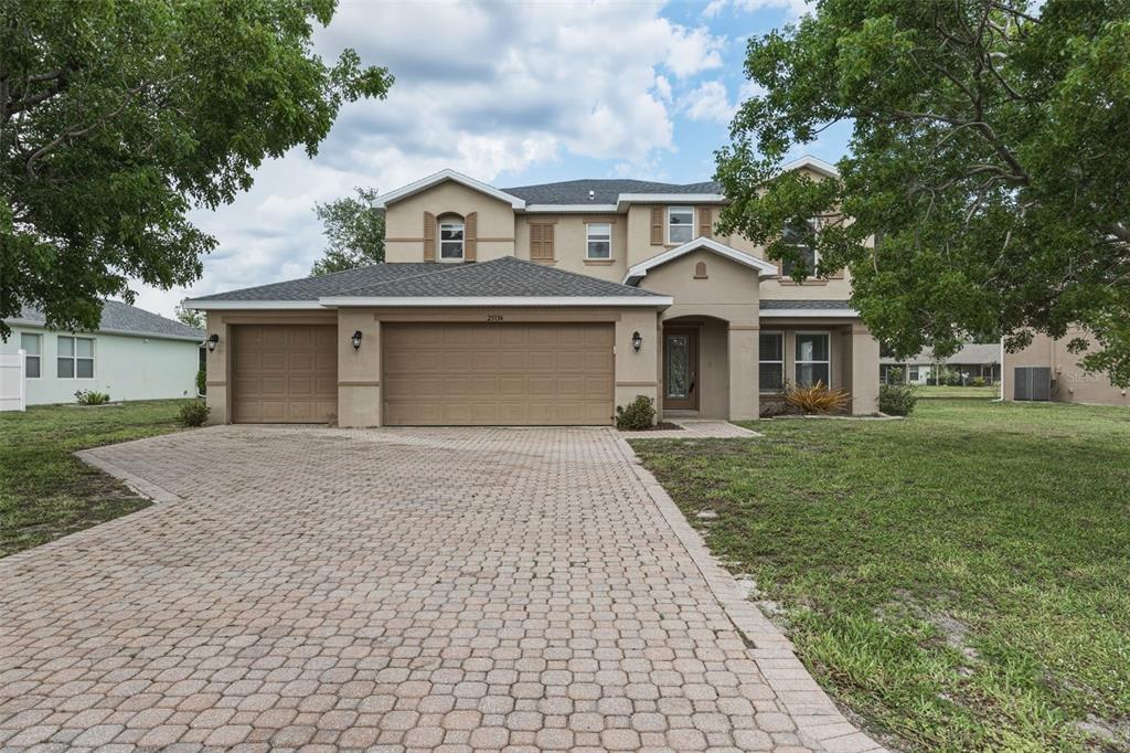 A two-story suburban house with a tan stucco exterior, a three-car garage, and a paver driveway — 25134 PALISADE ROAD, PUNTA GORDA, FL