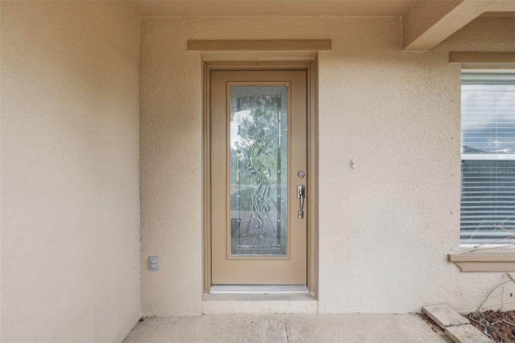 A beige front door with a decorative glass insert is set into a stucco exterior wall — 25134 PALISADE ROAD, PUNTA GORDA, FL