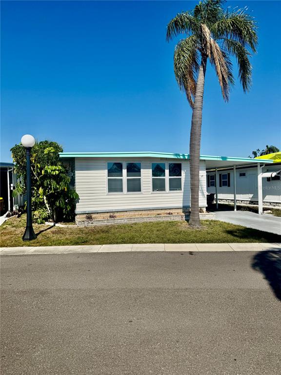 A single-story mobile home features light siding, a palm tree, and an attached carport — 7901 N 40TH AVENUE N UNIT 21, ST PETERSBURG, FL
