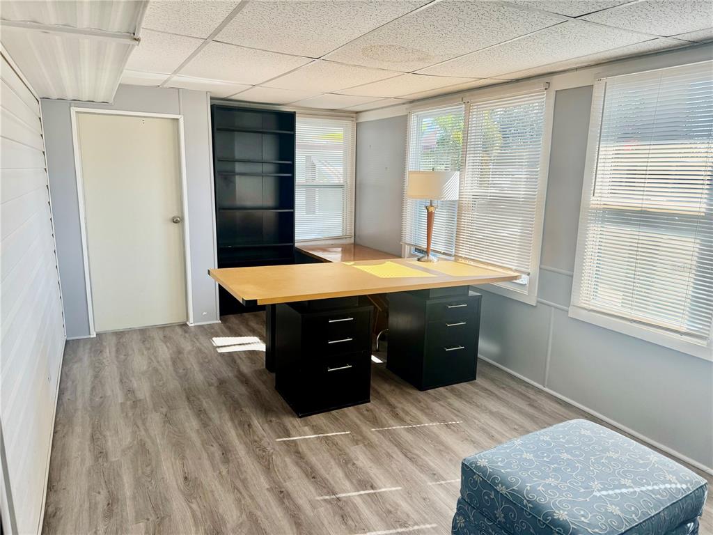 A home office with wood-look flooring, a large desk, black storage units, and multiple windows — 7901 N 40TH AVENUE N UNIT 21, ST PETERSBURG, FL