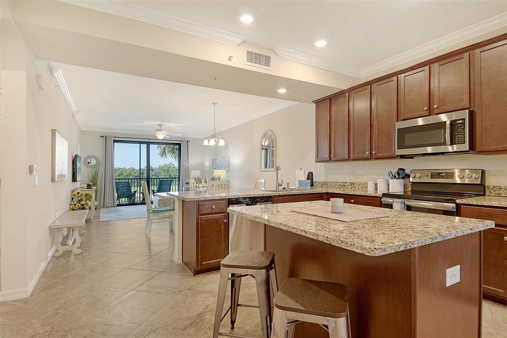 A kitchen with dark wood cabinets, granite countertops, and an island overlooks a living area — 17006 VARDON TERRACE UNIT 305, BRADENTON, FL