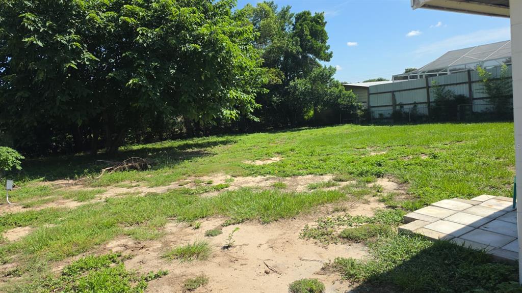 A grassy backyard features a large tree, sandy patches, and a white fence — 114 ANARECE AVENUE, AUBURNDALE, FL
