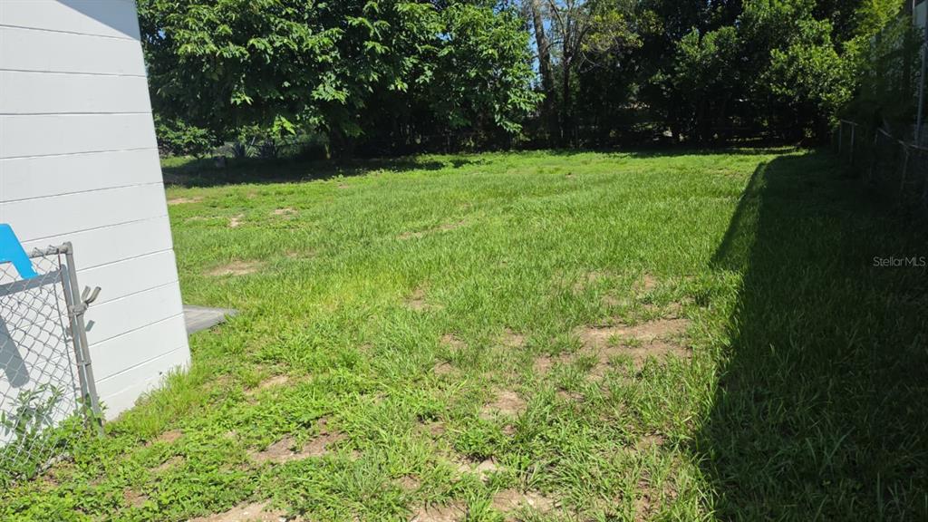 A grassy backyard area adjacent to a white building with a chain-link fence — 114 ANARECE AVENUE, AUBURNDALE, FL