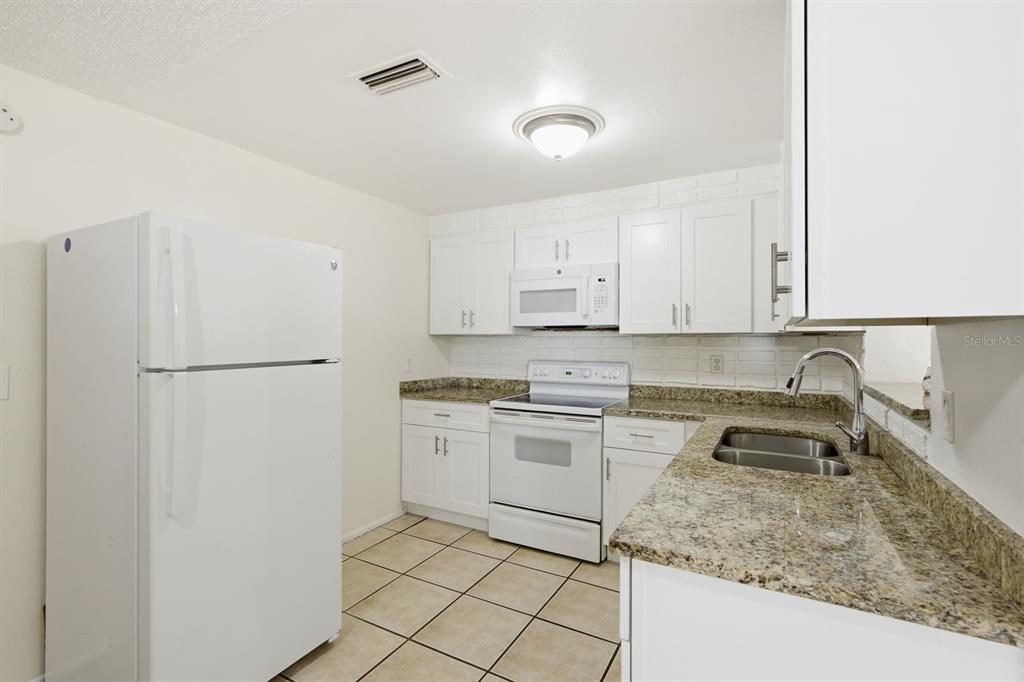 A kitchen features white cabinets, granite countertops, white appliances, and light-colored tile flooring — 1119 17TH AVENUE SW, LARGO, FL