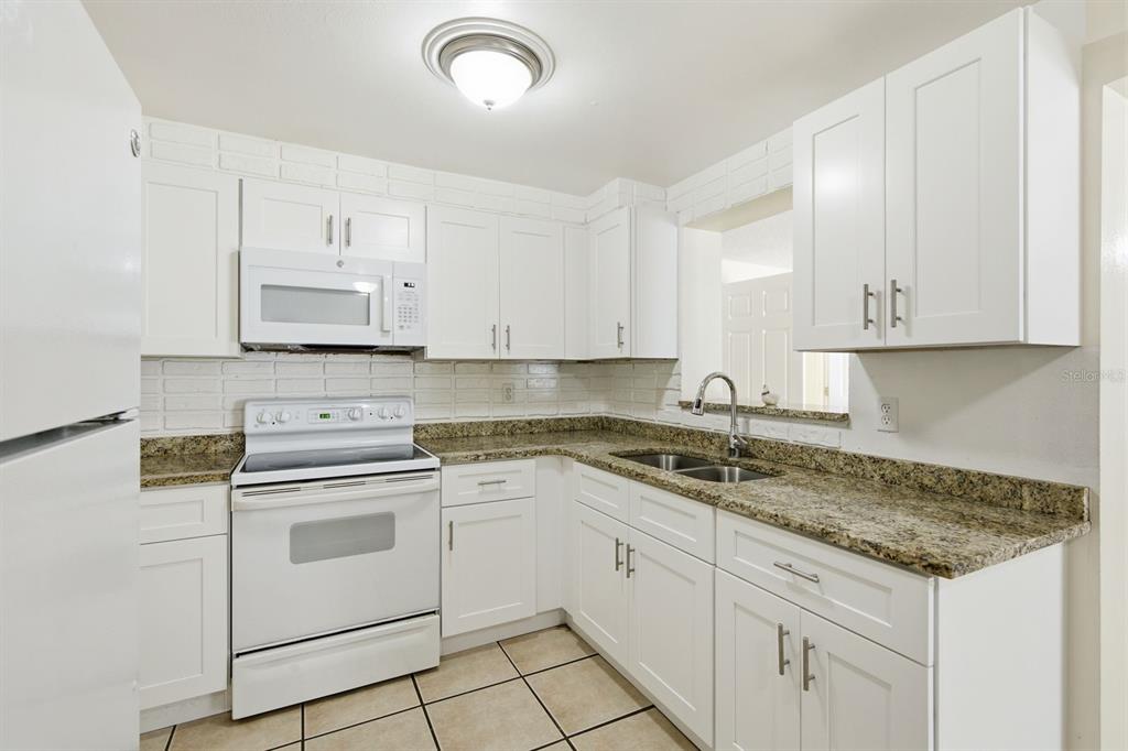 A kitchen with white cabinets, granite countertops, a white stove, and a brick backsplash — 1119 17TH AVENUE SW, LARGO, FL
