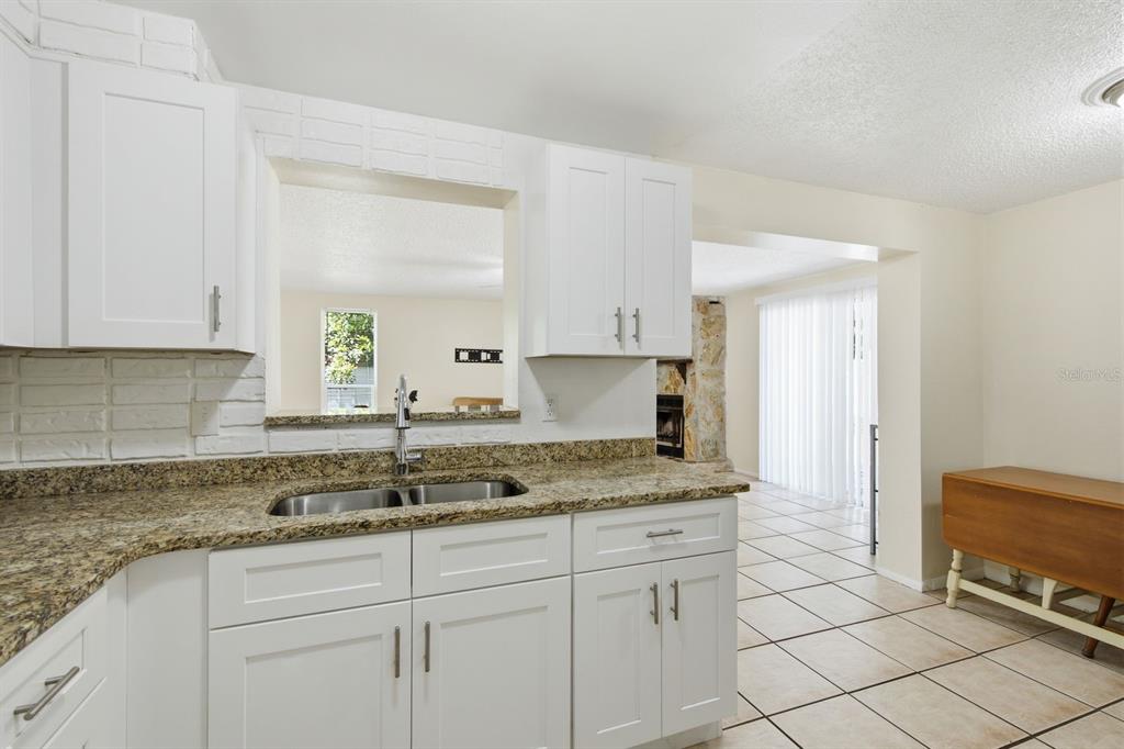 A kitchen with white cabinets, granite countertops, and a pass-through window overlooking the living area — 1119 17TH AVENUE SW, LARGO, FL