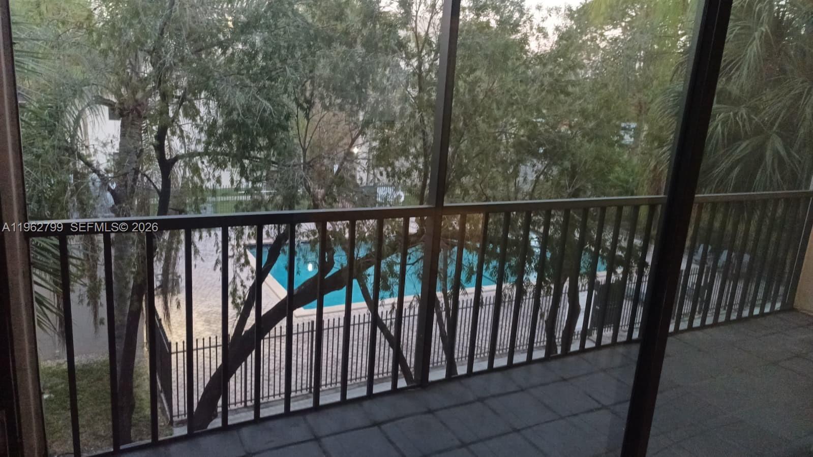 A view from a screened balcony overlooking a swimming pool surrounded by trees — 8400 SW 133rd Ave Rd # 318, Miami FL 33183, MIAMI, FL